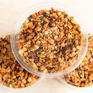Drei durchsichtige Plastikbehälter mit je 250 g Selbstgemachtes Granola (glutenfrei), gefüllt mit einer Mischung aus Hafer, Samen und Nüssen, sind von oben zu sehen.