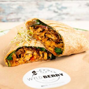 Ein Vollkorn-Falafel-Wrap, gefüllt mit geschreddertem Gemüse und Grünzeug, halbiert und auf braunem Papier mit einem "Wyld Berry"-Aufkleber serviert.